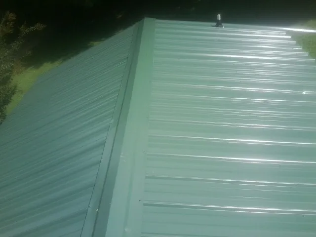 New green metal panels meeting at the ridge of a roof — Flat Roof Repair work by our crew in Pierce